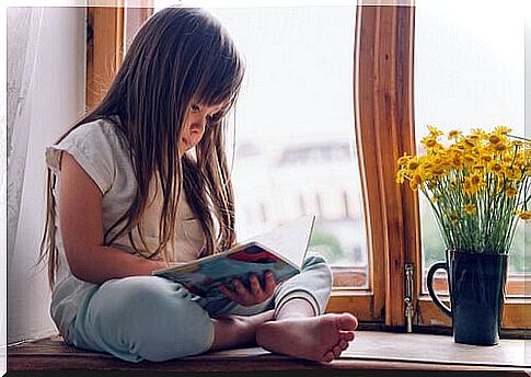 Little girl is reading sitting at the window