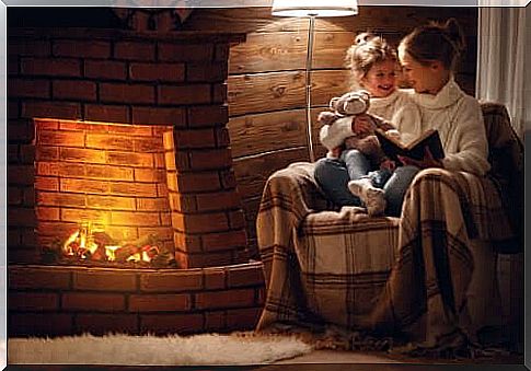 mother reading to her daughter a children's storybook sitting on the armchair in front of the fireplace
