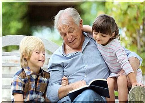 Grandfather sitting on a bench reading a book by Gianni Rodari to his grandchildren.