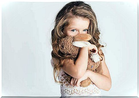 Shy little girl hiding behind a plush rabbit.